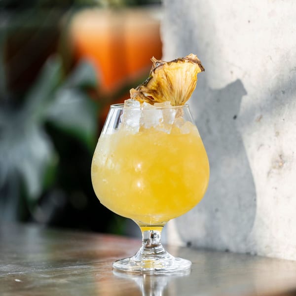 Paraiso's yellow cocktail with crushed ice and a dried pineapple garnish on a wooden table.