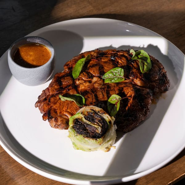 Grilled steak with charred cabbage and a side of sauce on a white plate.