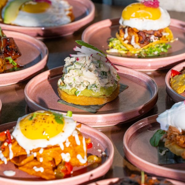 Several pink plates filled with various Mexican dishes, including nachos, tostadas, and fried eggs.