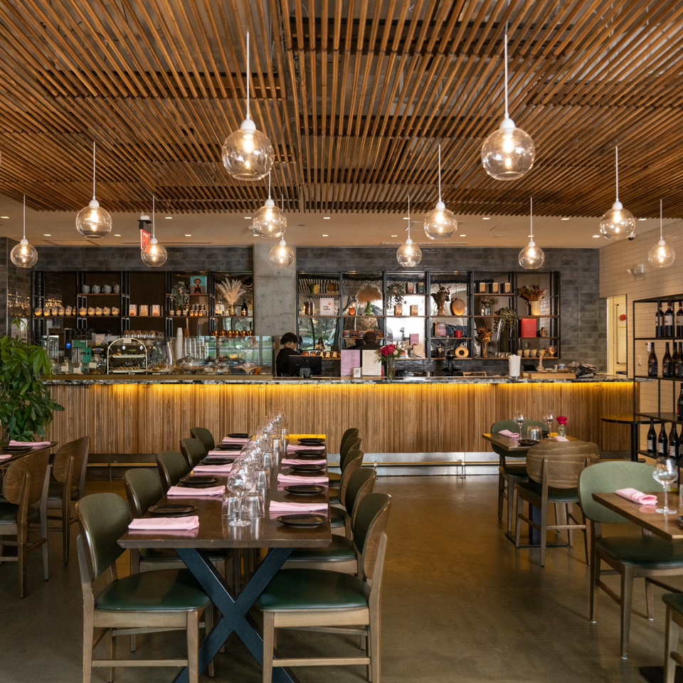 Warmly lit restaurant dining room with set tables, a wooden slatted ceiling, pendant lights, and a visible bar.