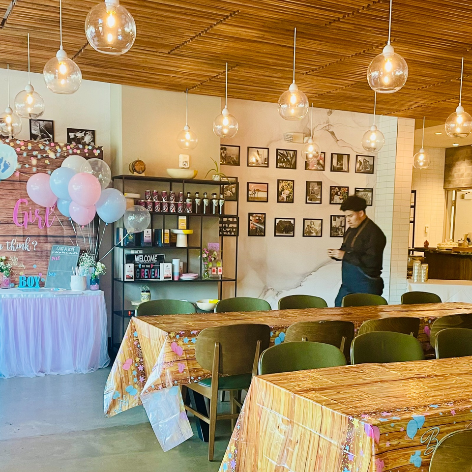 Warm restaurant interior with pendant lights, framed artwork, decorated tables, balloons, and a person near the bar.