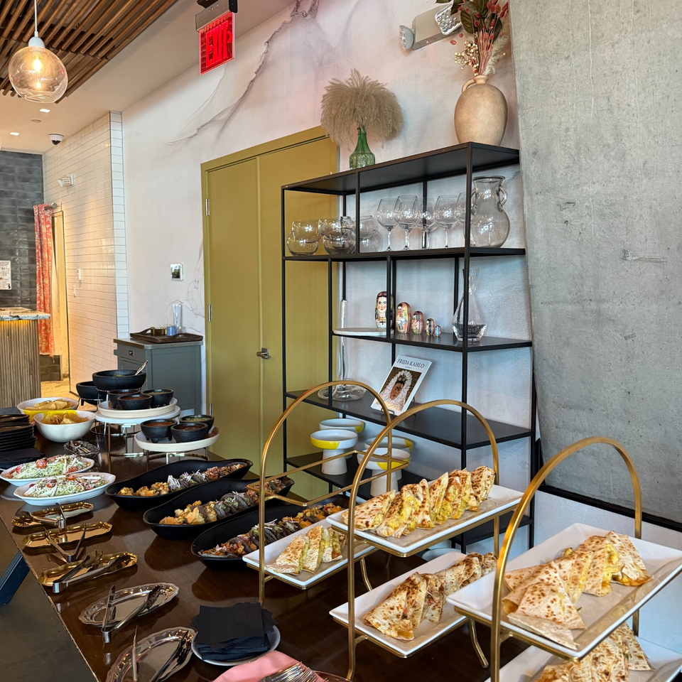 Restaurant buffet displays folded flatbreads, assorted dishes, serving utensils, and glassware beneath modern shelving.