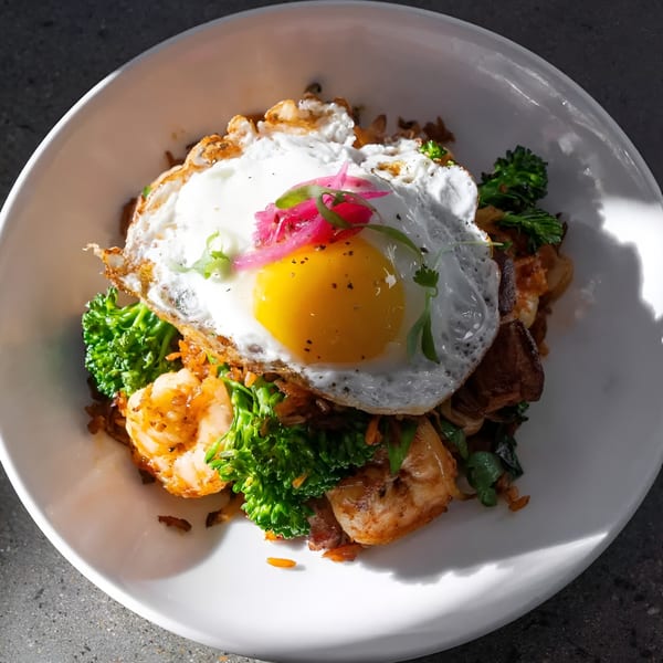 Mexican dish with fried egg, shrimp, broccoli, and pickled onions in a white bowl.